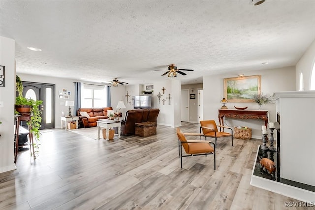 living area with ceiling fan, baseboards, light wood finished floors, and a textured ceiling