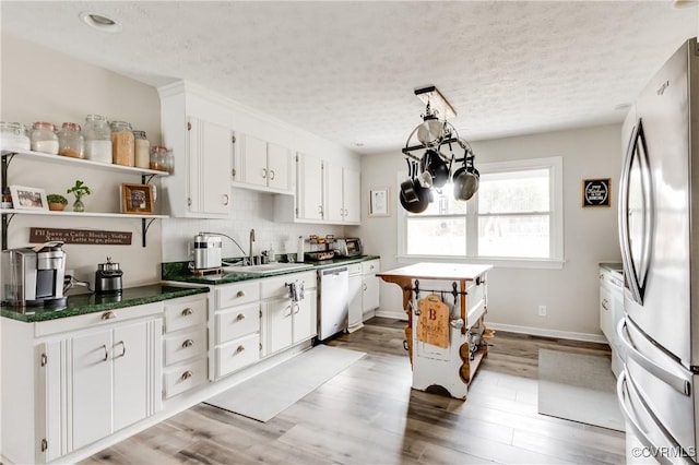 kitchen with white dishwasher, freestanding refrigerator, a sink, white cabinetry, and dark countertops