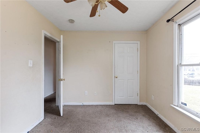 unfurnished bedroom featuring carpet floors, multiple windows, a ceiling fan, and baseboards