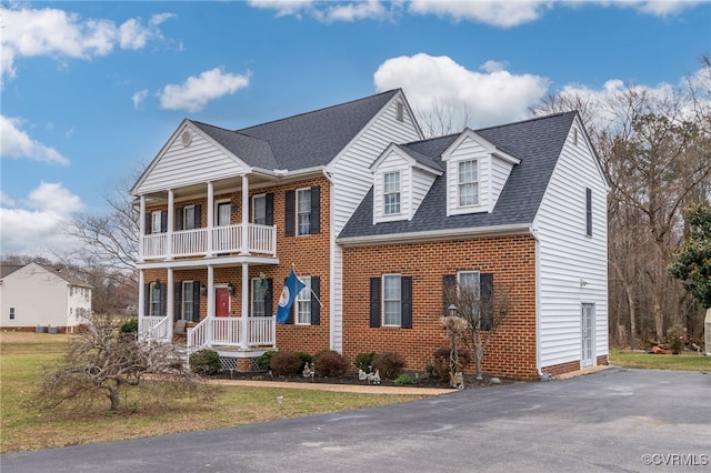 greek revival inspired property with a shingled roof, covered porch, brick siding, and a balcony