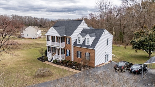 view of front of property with brick siding, covered porch, a balcony, driveway, and a front lawn