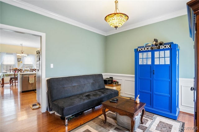 sitting room featuring a wainscoted wall, wood finished floors, crown molding, a decorative wall, and a notable chandelier