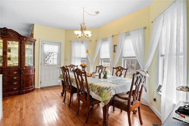 dining area with a wealth of natural light, light wood-type flooring, a chandelier, and baseboards