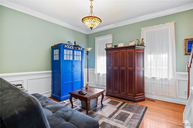 living area with light wood-type flooring, visible vents, ornamental molding, and wainscoting