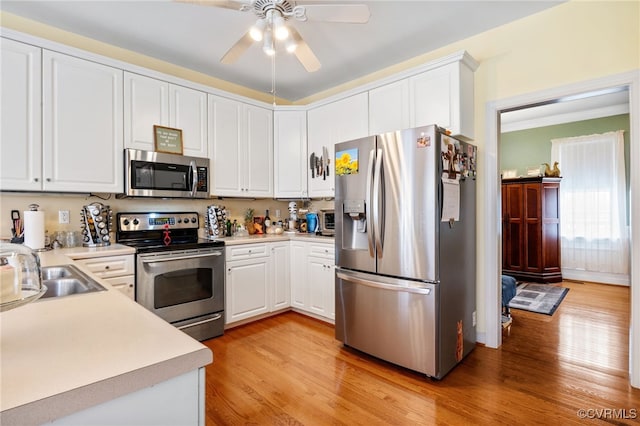 kitchen with appliances with stainless steel finishes, light wood-type flooring, light countertops, and white cabinetry