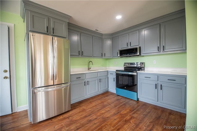 kitchen featuring appliances with stainless steel finishes, dark wood-style flooring, light countertops, gray cabinetry, and a sink