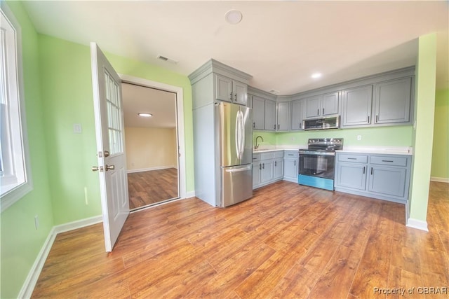 kitchen featuring stainless steel appliances, visible vents, light wood-style floors, light countertops, and gray cabinets