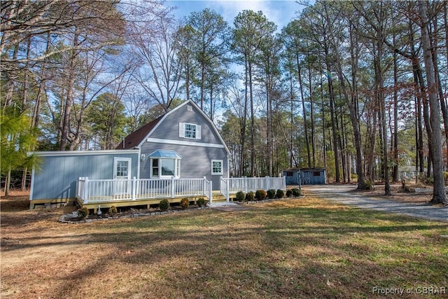 view of front facade with a gambrel roof, a deck, an outdoor structure, a shed, and a front lawn