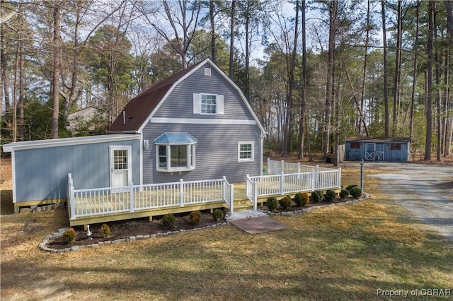 back of property with an outdoor structure, a lawn, a wooden deck, and a gambrel roof