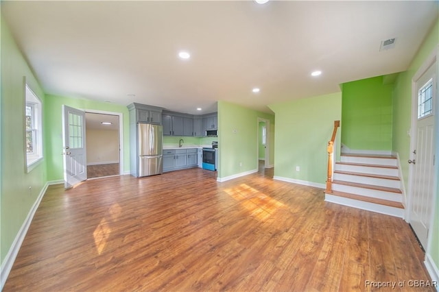 unfurnished living room featuring recessed lighting, visible vents, baseboards, stairway, and light wood finished floors