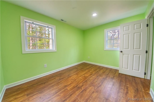 empty room featuring wood finished floors, visible vents, and baseboards