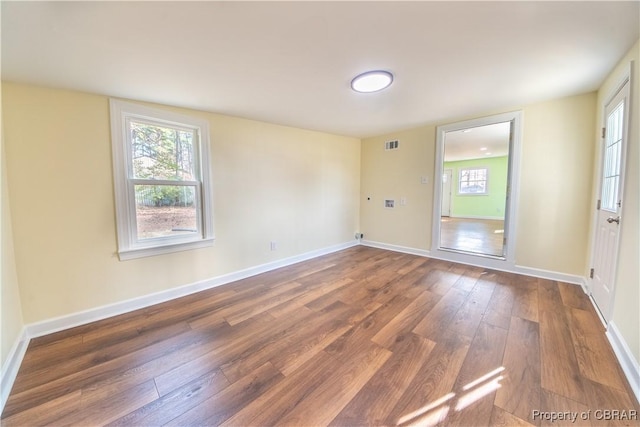 spare room with baseboards, wood-type flooring, visible vents, and a wealth of natural light