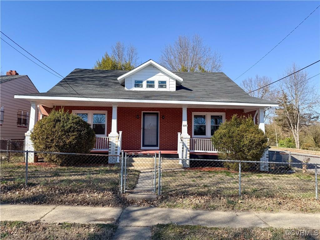 bungalow featuring a fenced front yard, brick siding, covered porch, and a gate