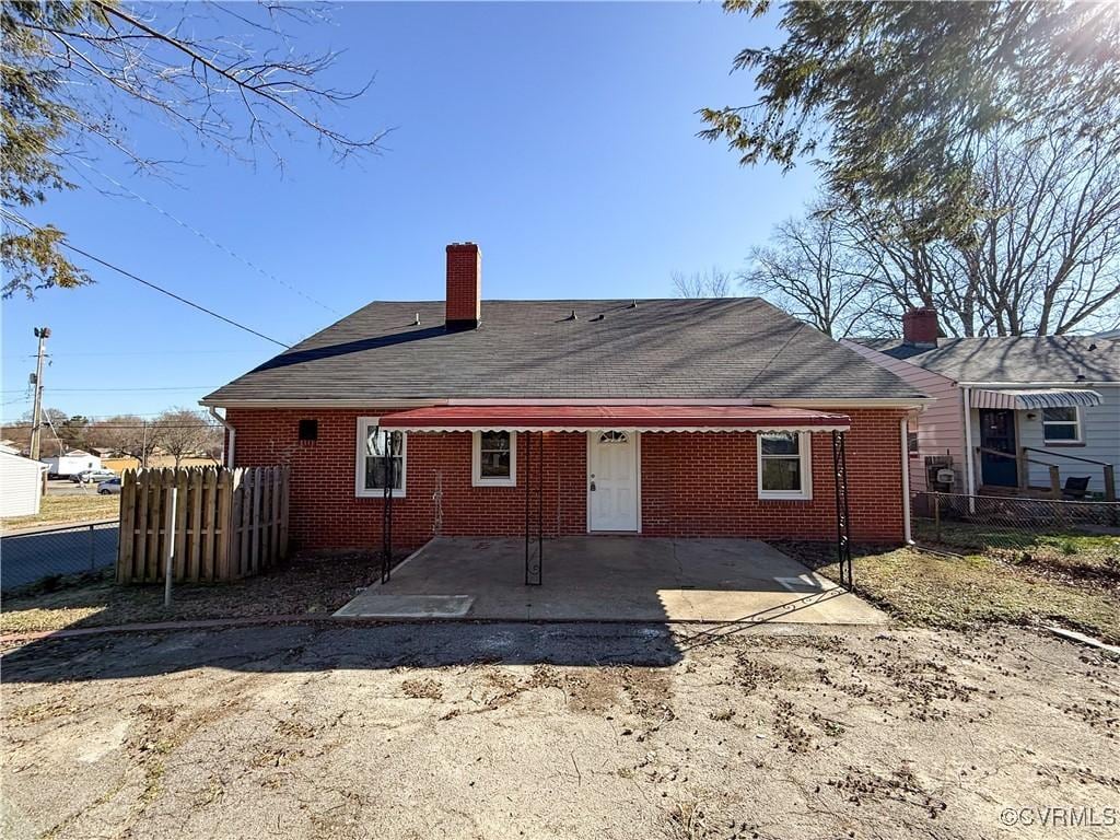 back of house featuring brick siding, a chimney, roof with shingles, and fence