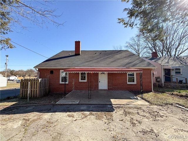 back of house featuring brick siding, a chimney, roof with shingles, and fence