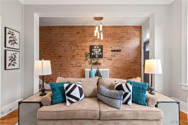 living area featuring radiator, wood finished floors, brick wall, and ornamental molding