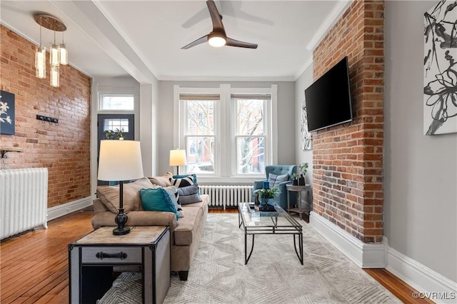 living room featuring radiator, brick wall, crown molding, and light wood-style floors