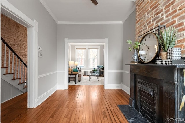 foyer featuring stairway, hardwood / wood-style floors, a large fireplace, and ornamental molding