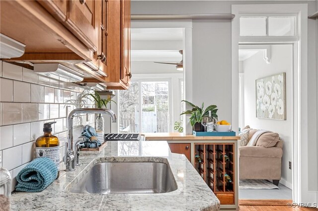 kitchen with brown cabinetry, backsplash, light stone countertops, and a sink