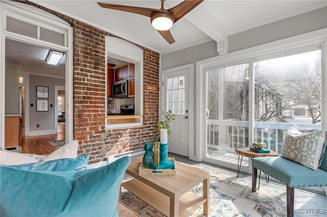 living area featuring brick wall, crown molding, beamed ceiling, wood finished floors, and a ceiling fan