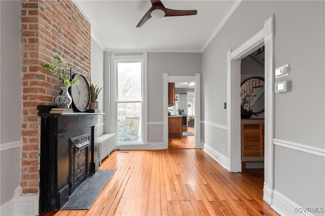 living room with radiator, a fireplace, ceiling fan, light wood-style floors, and crown molding