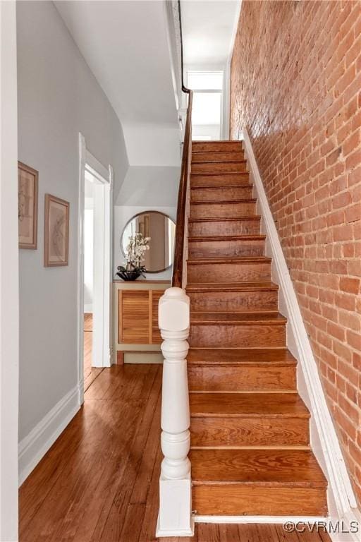 stairway featuring baseboards, wood finished floors, and brick wall