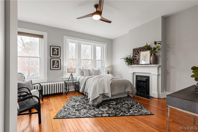 bedroom with hardwood / wood-style flooring, radiator, a fireplace with raised hearth, and ceiling fan