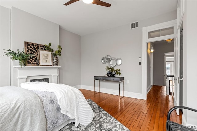 bedroom with hardwood / wood-style floors, a ceiling fan, baseboards, visible vents, and a fireplace