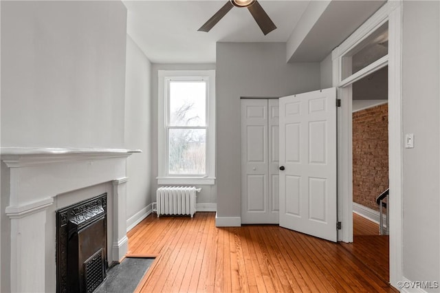 unfurnished living room featuring a fireplace with flush hearth, hardwood / wood-style floors, radiator, baseboards, and ceiling fan