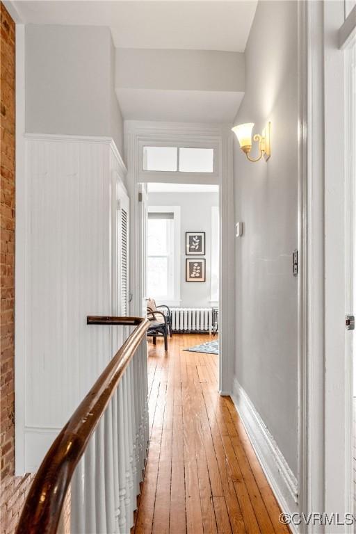 corridor featuring radiator heating unit, brick wall, an upstairs landing, and light wood finished floors