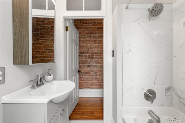 full bathroom featuring vanity, wood finished floors, baseboards, brick wall, and shower / bath combination