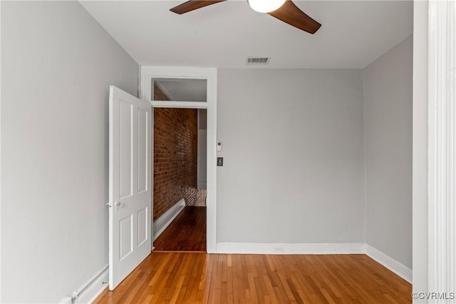 spare room featuring a ceiling fan, visible vents, brick wall, baseboards, and light wood-style floors