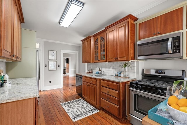 kitchen with brown cabinets, stainless steel appliances, wood-type flooring, crown molding, and decorative backsplash