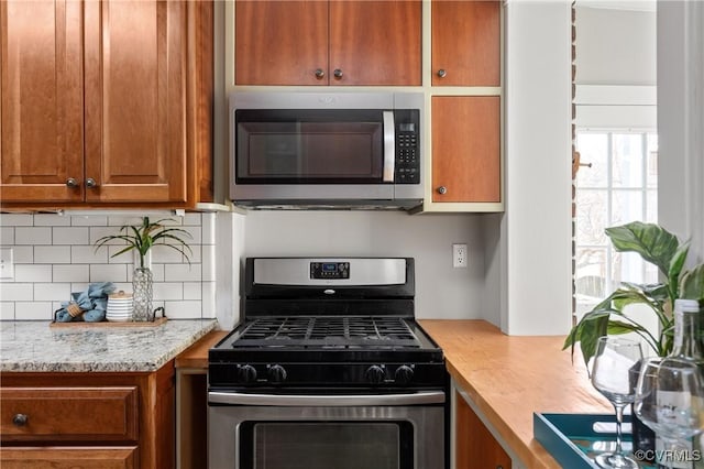 kitchen featuring light stone counters, brown cabinetry, tasteful backsplash, and stainless steel appliances