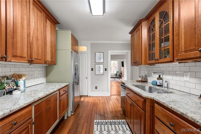 kitchen featuring glass insert cabinets, baseboards, brown cabinets, appliances with stainless steel finishes, and a sink