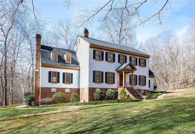 view of front of house with brick siding, a chimney, and a front lawn