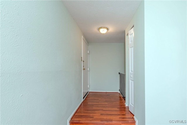 hall with baseboards, a textured ceiling, and wood finished floors