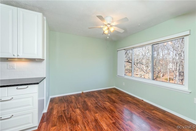 unfurnished dining area featuring baseboards, dark wood-style flooring, and ceiling fan