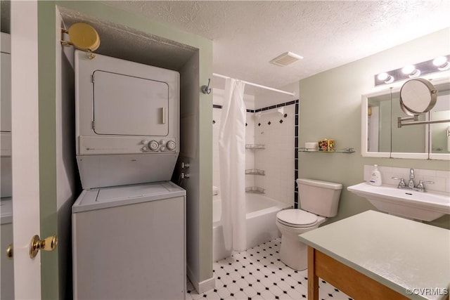 bathroom featuring visible vents, stacked washing maching and dryer, shower / bath combo with shower curtain, a textured ceiling, and toilet