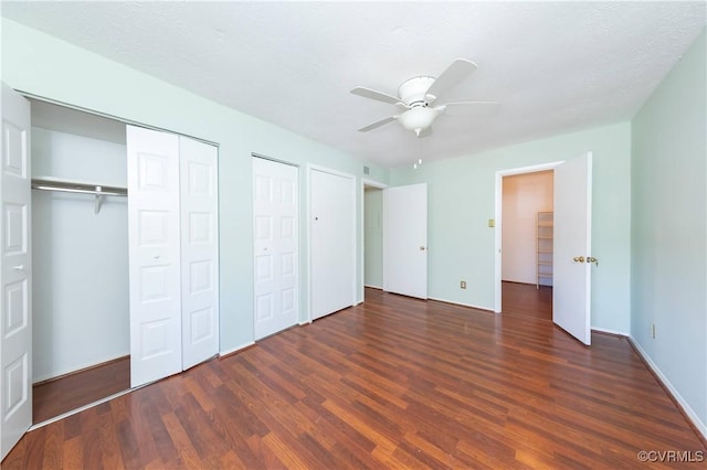 unfurnished bedroom featuring baseboards, a ceiling fan, multiple closets, and wood finished floors