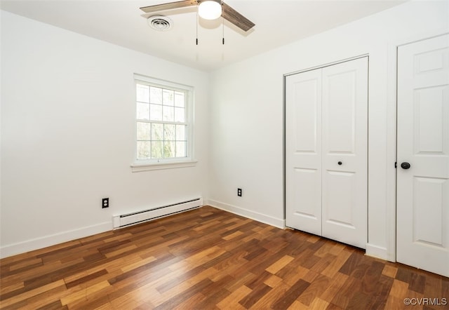 unfurnished bedroom with a closet, visible vents, baseboard heating, wood finished floors, and baseboards