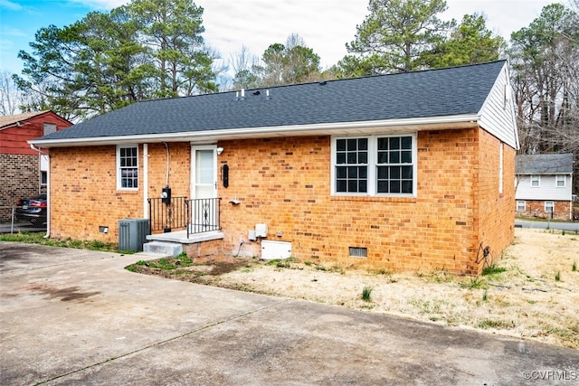 view of front facade featuring crawl space, a shingled roof, central AC unit, and brick siding