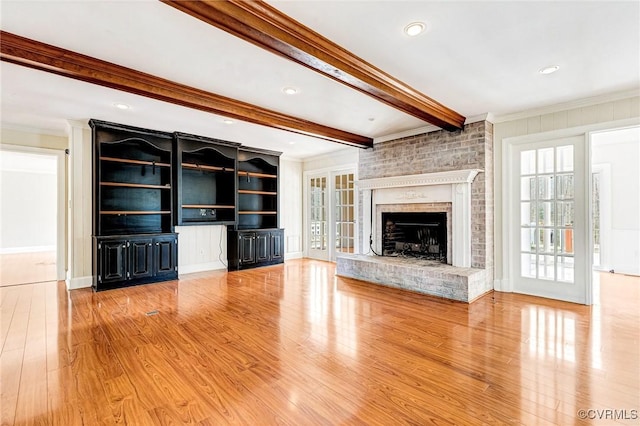 unfurnished living room with light wood-style floors, crown molding, a fireplace, and beam ceiling