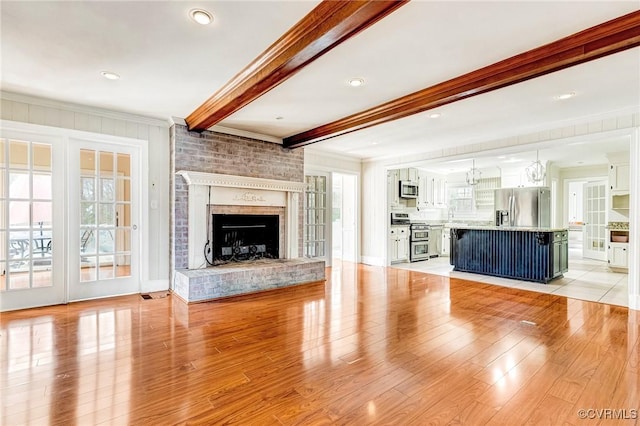 unfurnished living room with ornamental molding, a brick fireplace, beam ceiling, and light wood-style floors