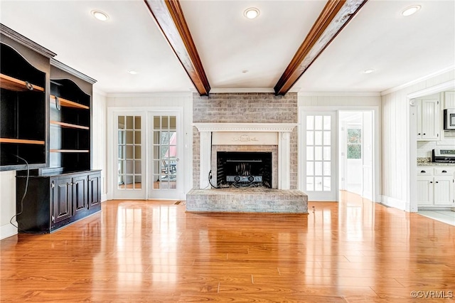 unfurnished living room with ornamental molding, light wood-type flooring, beam ceiling, and a brick fireplace