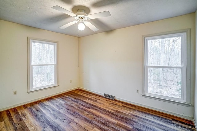 spare room featuring a healthy amount of sunlight, a textured ceiling, visible vents, and wood finished floors