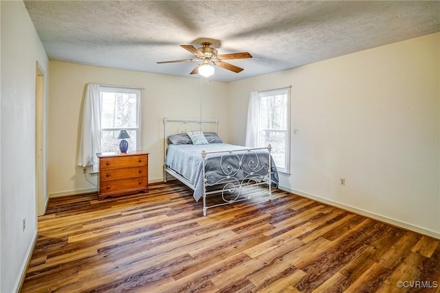 bedroom with a textured ceiling, multiple windows, baseboards, and wood finished floors