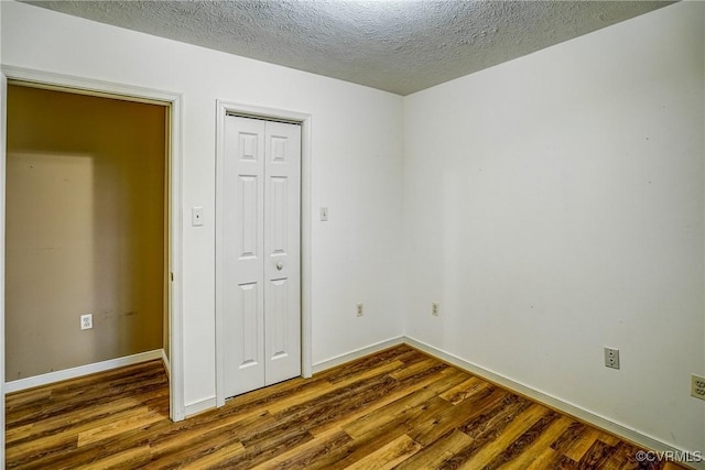 unfurnished bedroom with a textured ceiling, a closet, dark wood finished floors, and baseboards