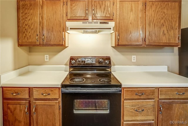 kitchen with brown cabinets, under cabinet range hood, light countertops, and black electric range oven