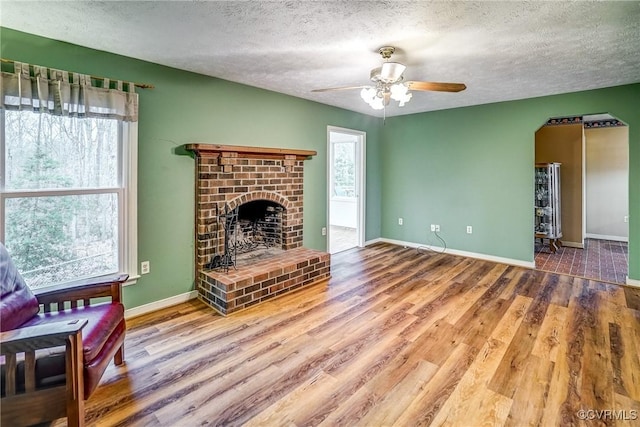 living area featuring a fireplace, ceiling fan, a textured ceiling, wood finished floors, and baseboards